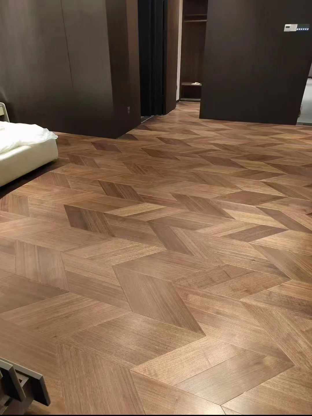Geometric parquet flooring with contrasting wood-grain directions beside dark wall panels