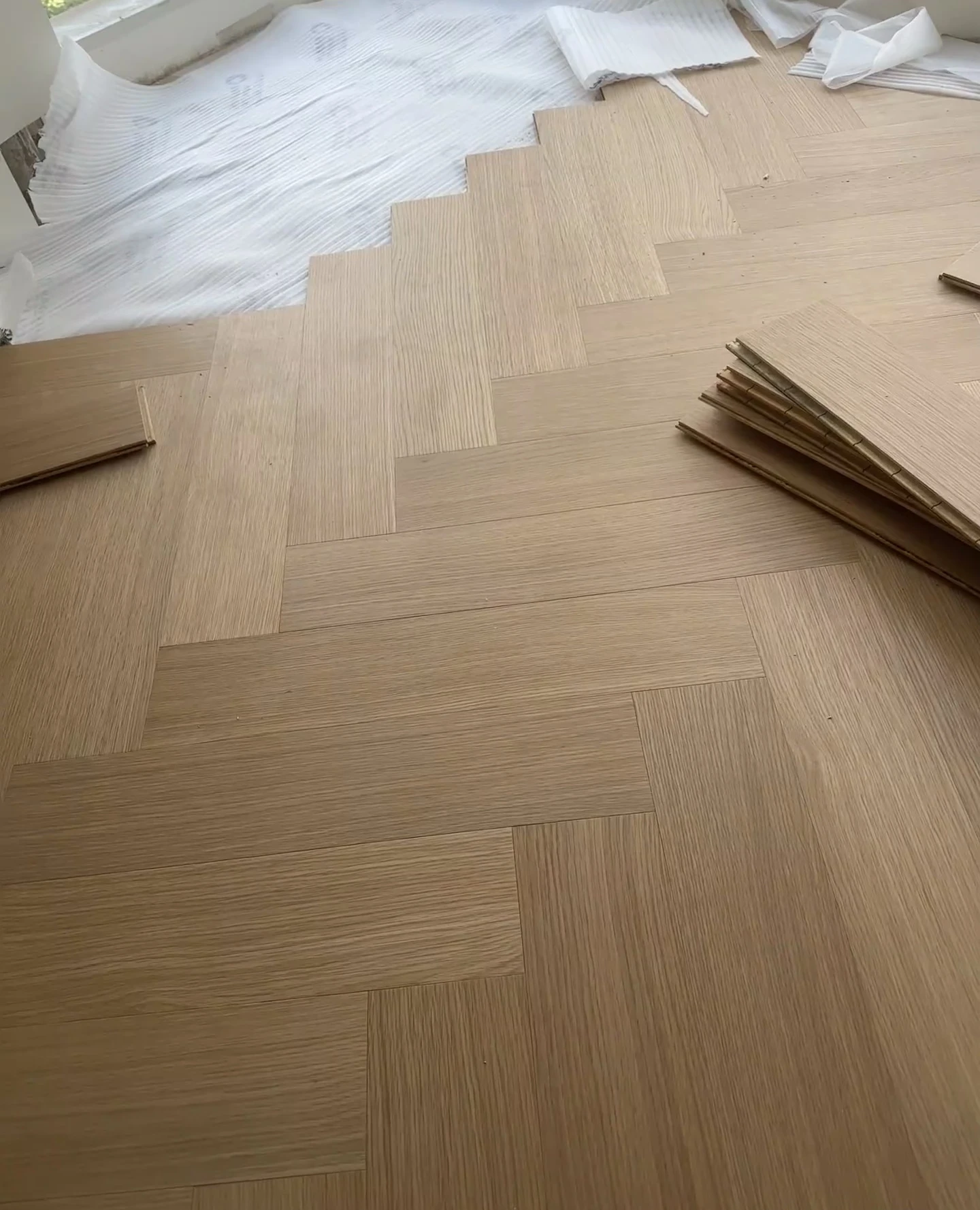 Light-toned herringbone flooring during laying, with loose boards and exposed underlay