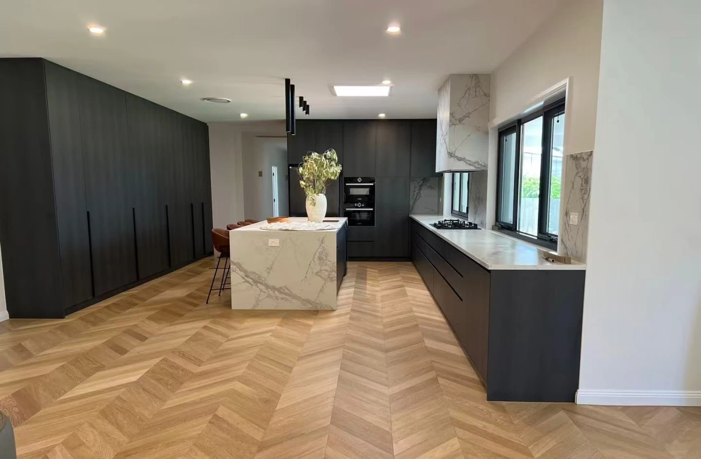 Warm-toned herringbone flooring around a stone island and dark kitchen cabinets