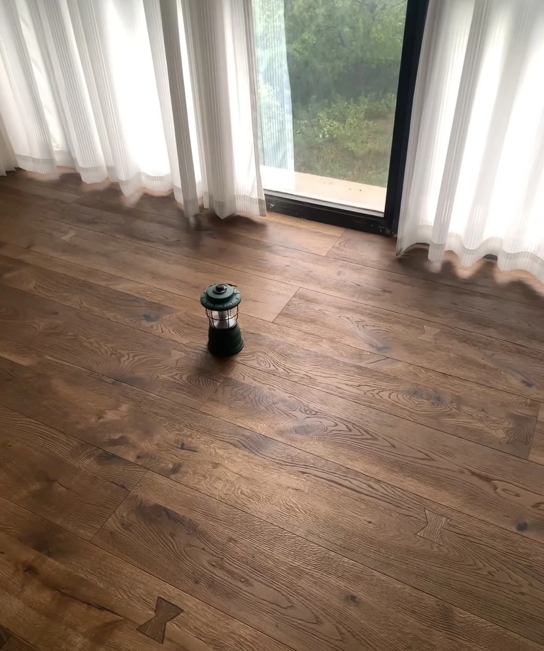 Brown straight-laid floorboards with visible knots and grain beside a curtained window