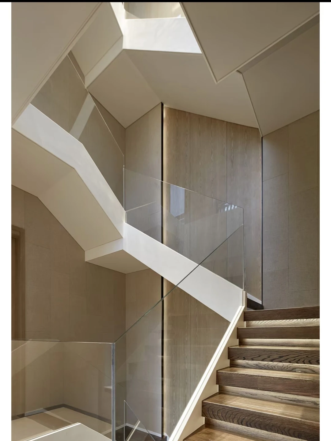 Frameless glass balustrade above white stair stringers with wood treads and tall timber wall panels