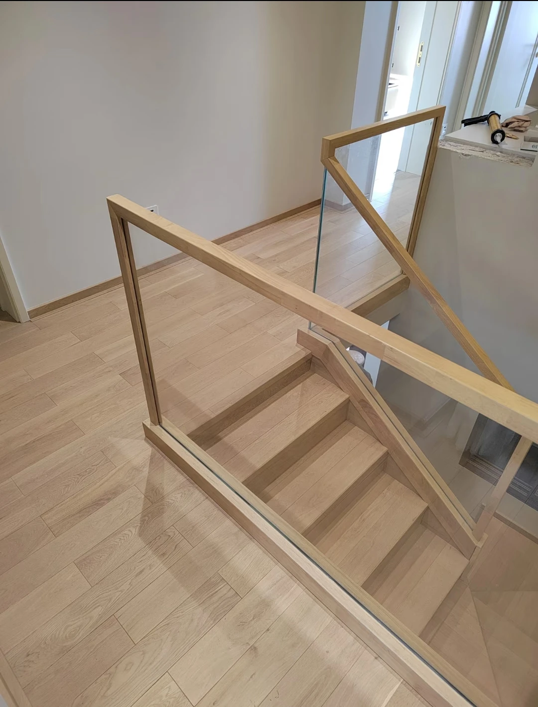 Light wood handrail and posts framing clear glass panels beside matching wood stair treads