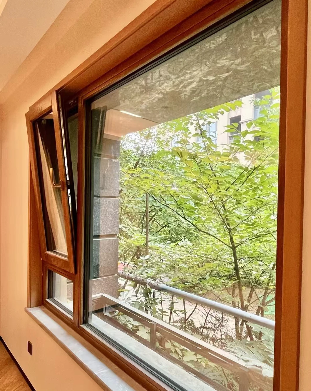 Wide picture window beside a narrow tilted-open panel, with wood-tone frames and a garden view