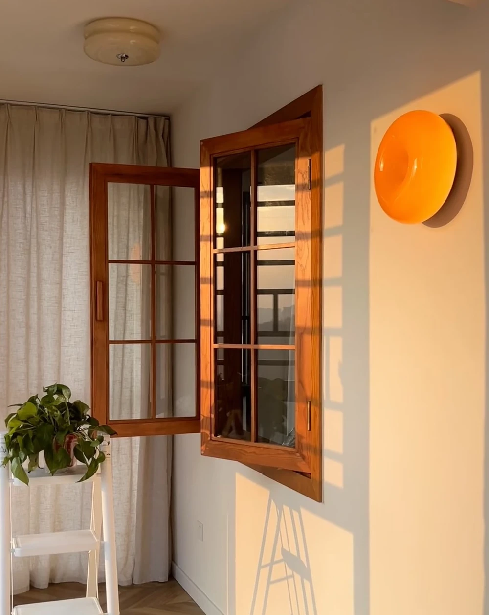Open side-hinged wood-tone casement window with divided panes in a sunlit room