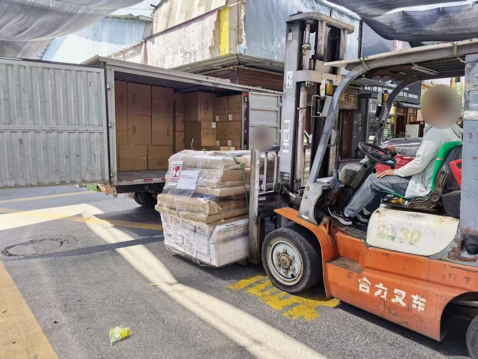 Forklift carrying a stretch-wrapped pallet of door and window packs into a box truck