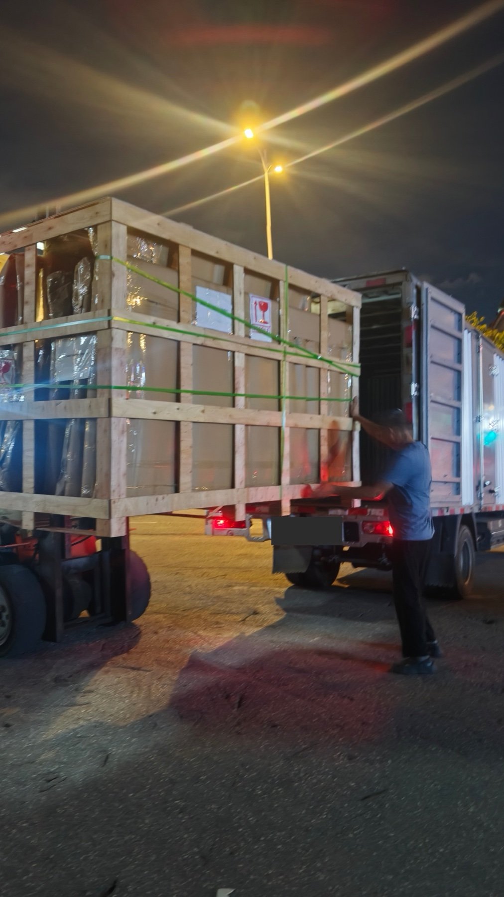 Timber-framed shutter package secured with straps during truck loading, with vehicle registration hidden