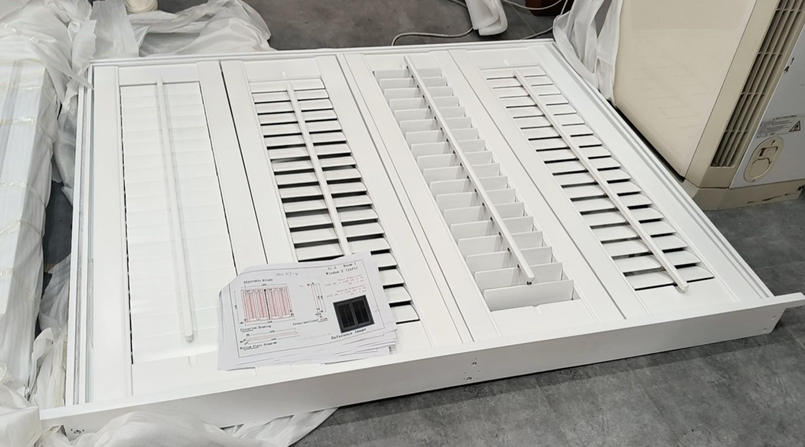 White wood plantation shutters with louvers at different angles and an individual project drawing beside the frame